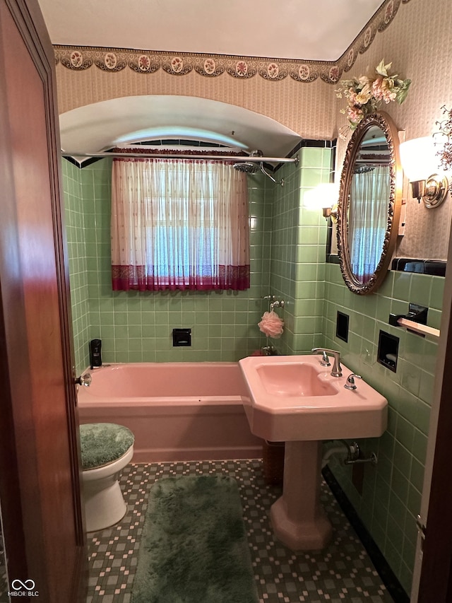 bathroom with tile walls, toilet, a bathing tub, and tile patterned floors