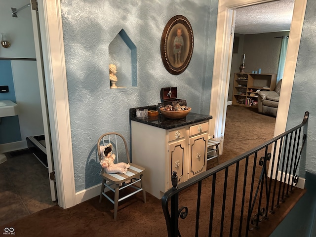 hallway with a textured ceiling and dark carpet