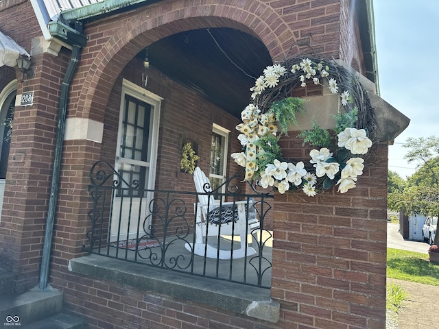 view of exterior entry with a porch and brick siding