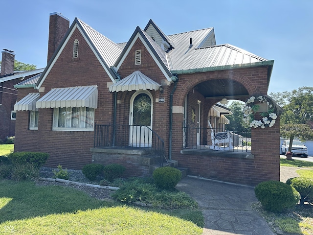 english style home with a standing seam roof, metal roof, brick siding, and a chimney