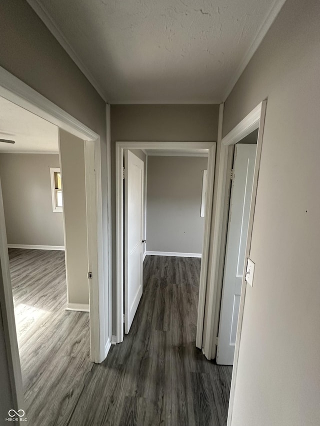 hallway with baseboards, a textured ceiling, dark wood finished floors, and crown molding