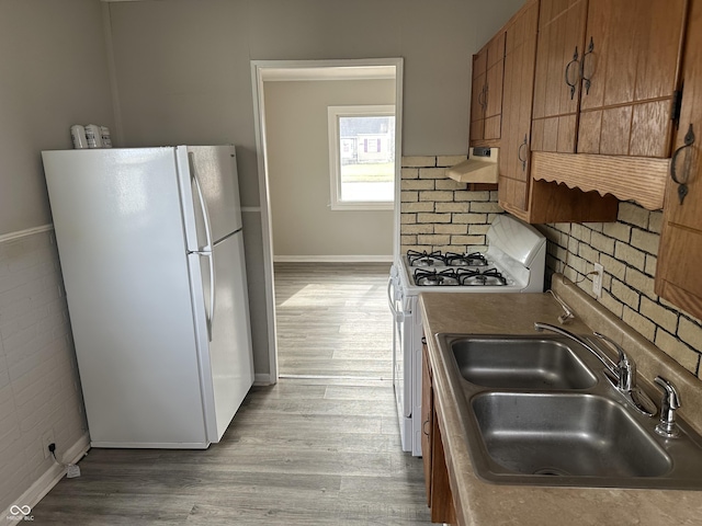 kitchen with brown cabinets, a sink, range hood, wood finished floors, and white appliances