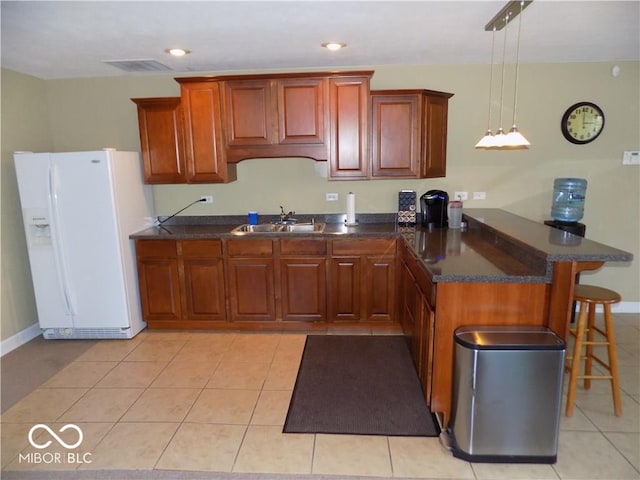 kitchen featuring a kitchen bar, sink, white fridge with ice dispenser, decorative light fixtures, and light tile patterned floors