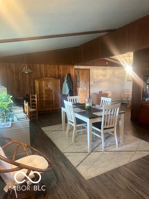 dining room featuring vaulted ceiling, wood-type flooring, and wooden walls