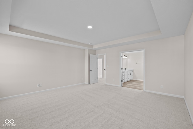 unfurnished bedroom with connected bathroom, light carpet, and a raised ceiling