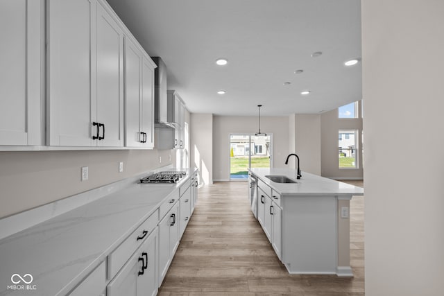 kitchen with wall chimney range hood, light hardwood / wood-style flooring, a center island with sink, sink, and white cabinetry