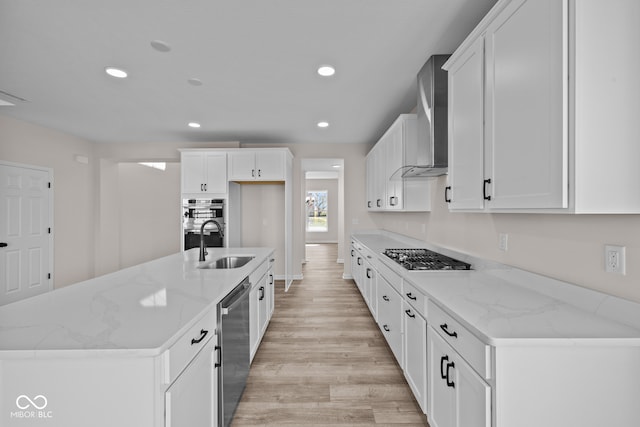 kitchen featuring light wood-type flooring, an island with sink, white cabinetry, stainless steel appliances, and wall chimney exhaust hood