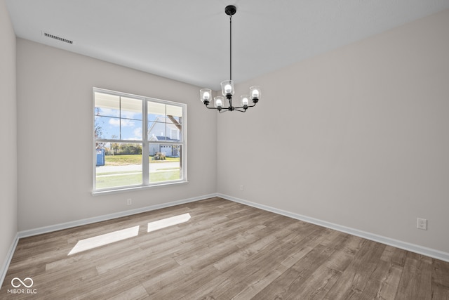 spare room featuring a notable chandelier and light wood-type flooring