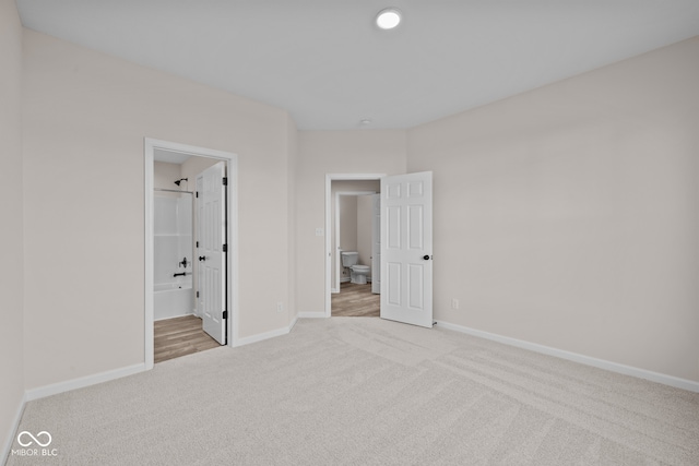 unfurnished bedroom featuring ensuite bathroom and light colored carpet