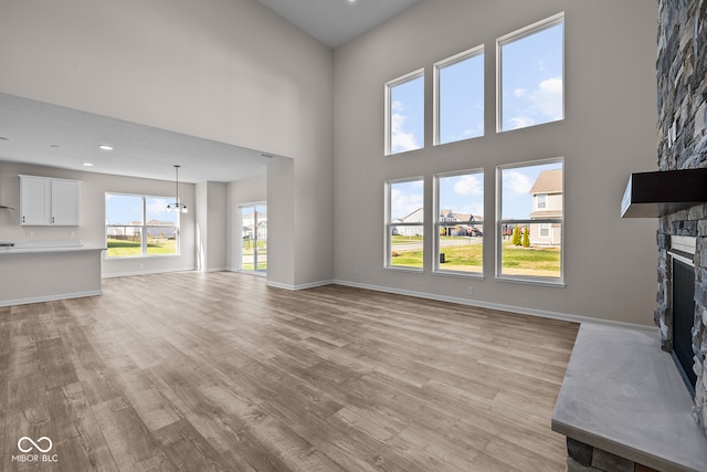 unfurnished living room with a high ceiling, light hardwood / wood-style flooring, a fireplace, and plenty of natural light