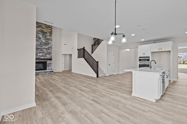 kitchen featuring stainless steel double oven, a kitchen island with sink, light hardwood / wood-style flooring, hanging light fixtures, and white cabinetry