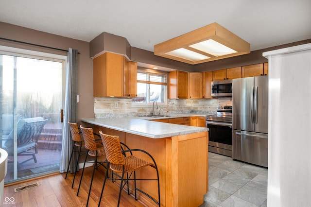 kitchen featuring a breakfast bar, backsplash, sink, kitchen peninsula, and stainless steel appliances