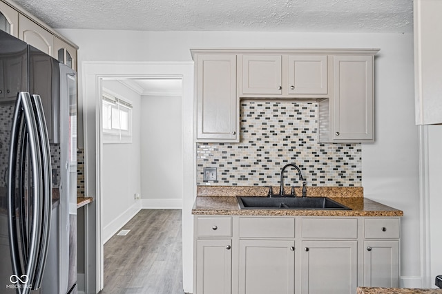 kitchen with backsplash, light hardwood / wood-style flooring, stainless steel refrigerator, sink, and a textured ceiling