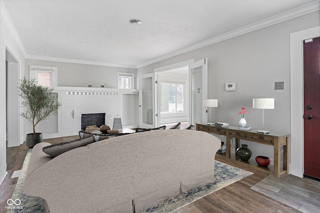 living room featuring wood-type flooring, ornamental molding, a textured ceiling, and a brick fireplace