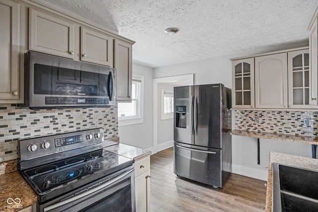 kitchen with a textured ceiling, stainless steel appliances, decorative backsplash, and light hardwood / wood-style floors