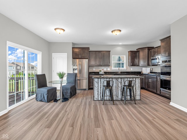 kitchen with dark brown cabinetry, appliances with stainless steel finishes, a kitchen breakfast bar, light wood-type flooring, and decorative backsplash