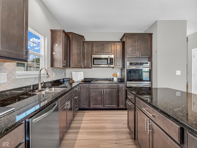 kitchen with appliances with stainless steel finishes, light hardwood / wood-style floors, tasteful backsplash, dark stone counters, and sink