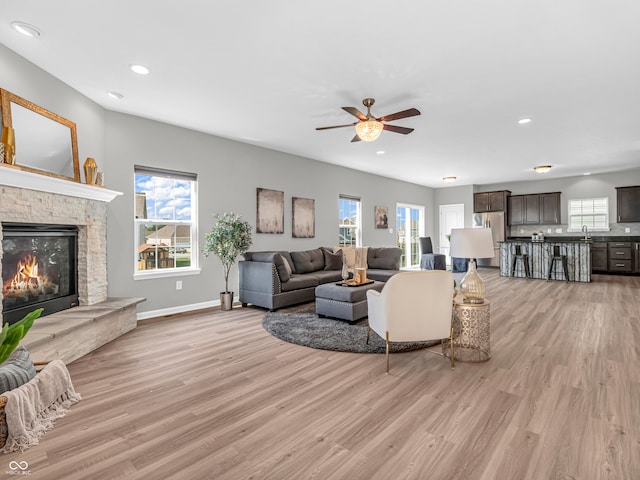 living room featuring light wood-type flooring, ceiling fan, plenty of natural light, and a fireplace