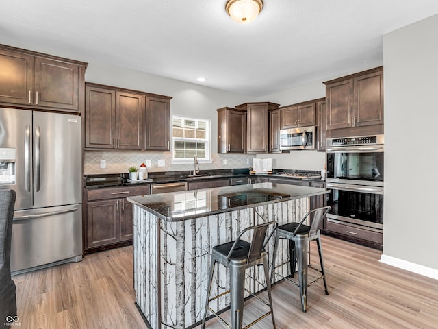 kitchen with appliances with stainless steel finishes, a breakfast bar area, light wood-type flooring, a center island, and sink