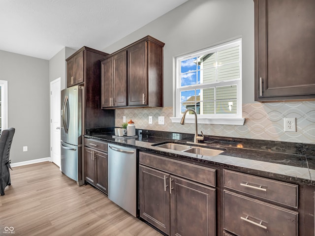 kitchen featuring dark brown cabinetry, sink, light hardwood / wood-style flooring, stainless steel appliances, and dark stone counters