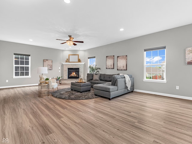 living room with ceiling fan, a stone fireplace, and light wood-type flooring