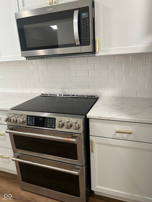 kitchen featuring dark hardwood / wood-style floors, light stone countertops, backsplash, appliances with stainless steel finishes, and white cabinets