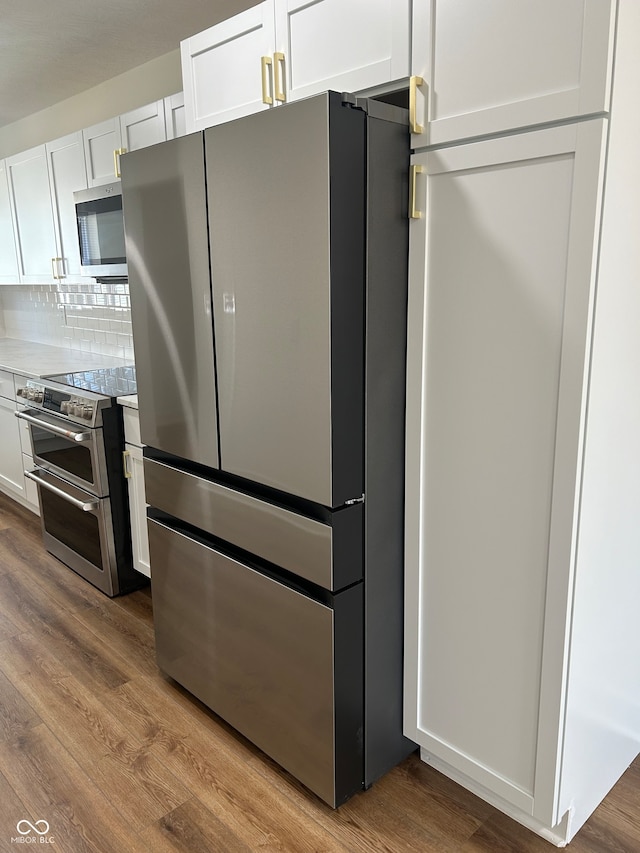 kitchen with appliances with stainless steel finishes, tasteful backsplash, hardwood / wood-style flooring, and white cabinets