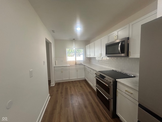 kitchen featuring backsplash, dark wood-type flooring, hanging light fixtures, appliances with stainless steel finishes, and white cabinets