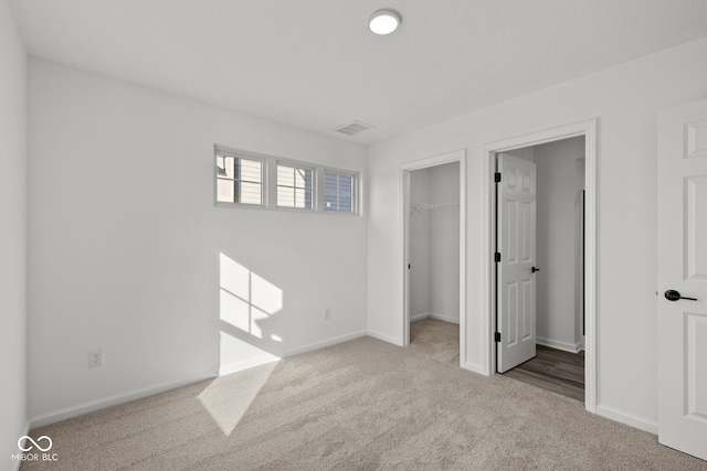 unfurnished bedroom featuring a walk in closet, a closet, and light colored carpet