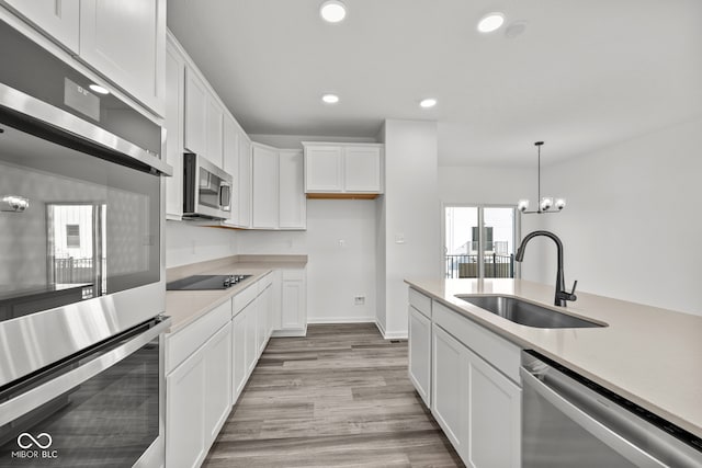 kitchen with appliances with stainless steel finishes, white cabinets, sink, and hanging light fixtures