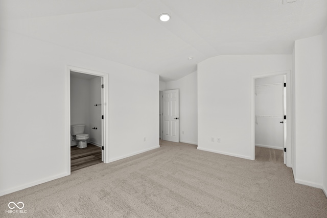 unfurnished bedroom with a spacious closet, lofted ceiling, light colored carpet, and ensuite bath