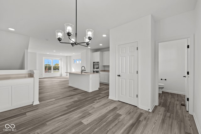 kitchen with sink, an island with sink, hanging light fixtures, white cabinetry, and light hardwood / wood-style floors