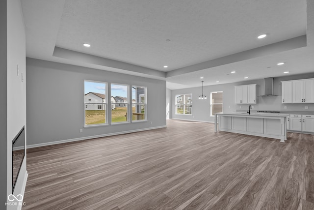 unfurnished living room with a textured ceiling, a raised ceiling, sink, an inviting chandelier, and light hardwood / wood-style floors