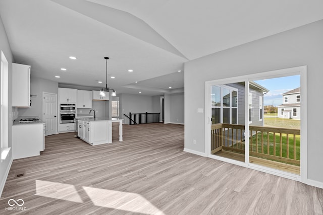 kitchen featuring light hardwood / wood-style floors, sink, decorative light fixtures, an island with sink, and white cabinets