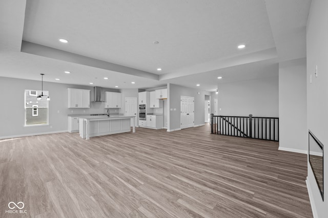 unfurnished living room with light hardwood / wood-style floors, an inviting chandelier, and a tray ceiling