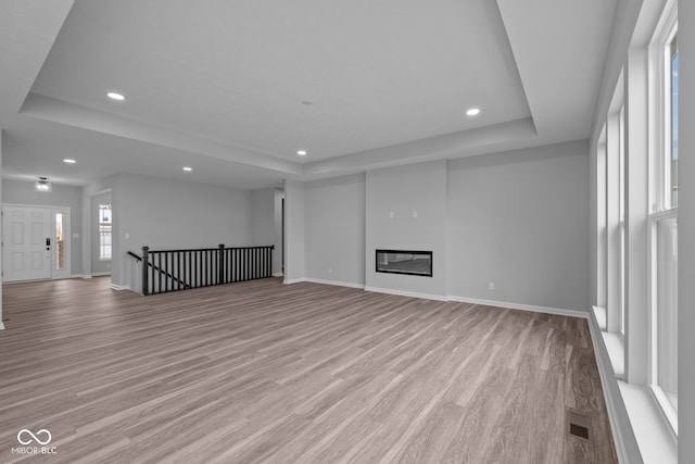 unfurnished living room with a raised ceiling and light hardwood / wood-style flooring