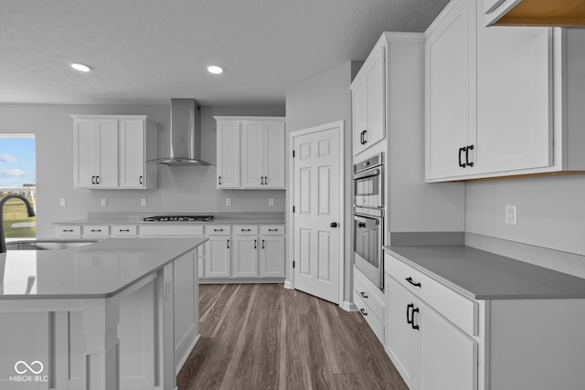 kitchen featuring white cabinetry, wall chimney range hood, and sink