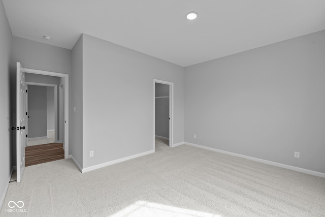 unfurnished bedroom with a closet, a spacious closet, and light colored carpet