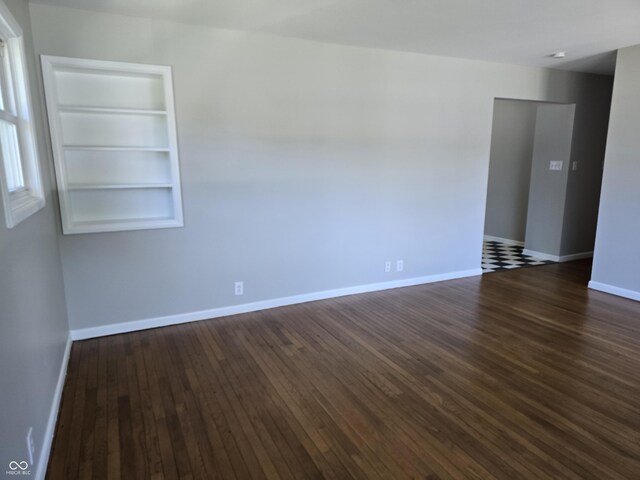 unfurnished room featuring dark wood-type flooring and built in shelves