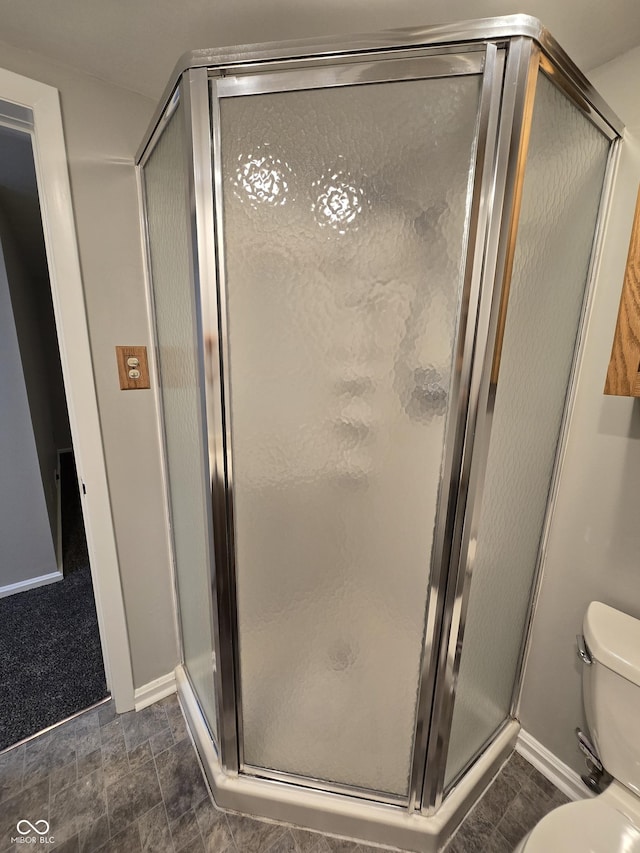 full bathroom with toilet, a stall shower, stone finish flooring, and baseboards