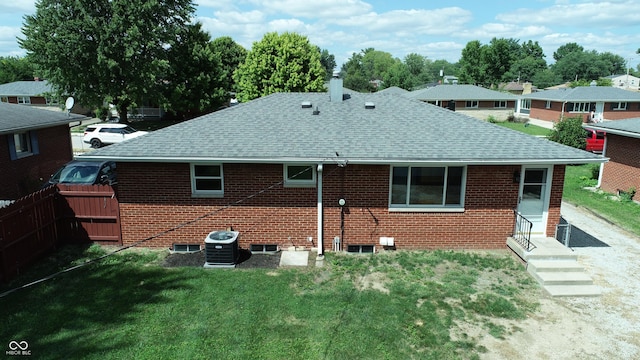 back of house featuring a shingled roof, brick siding, a lawn, and central AC