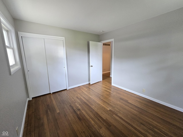 unfurnished bedroom featuring dark wood-style flooring, visible vents, and baseboards