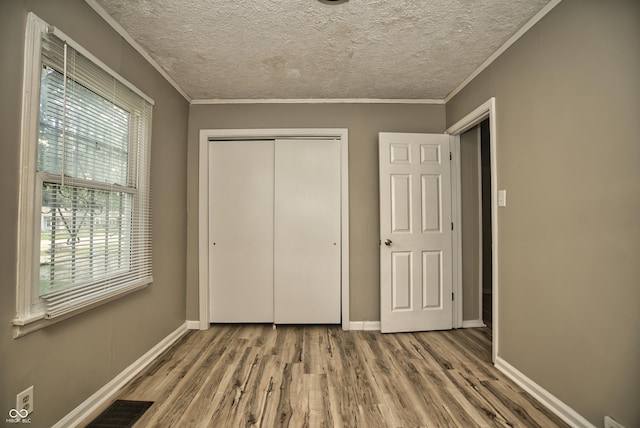 unfurnished bedroom with a textured ceiling, crown molding, baseboards, and wood finished floors