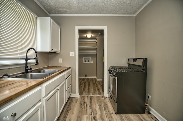 kitchen featuring a sink, a textured ceiling, light wood finished floors, wooden counters, and stainless steel range with gas stovetop