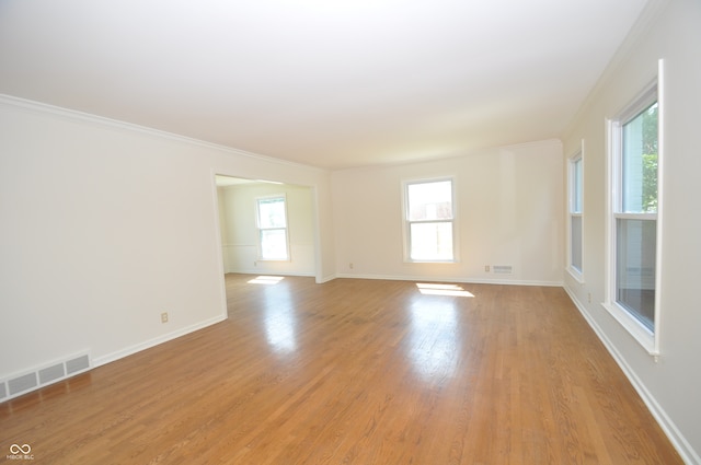 empty room with light wood-type flooring, visible vents, crown molding, and baseboards