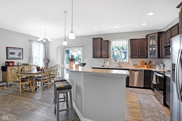 kitchen with dark brown cabinetry, a kitchen island, a kitchen breakfast bar, stainless steel appliances, and light wood-style floors