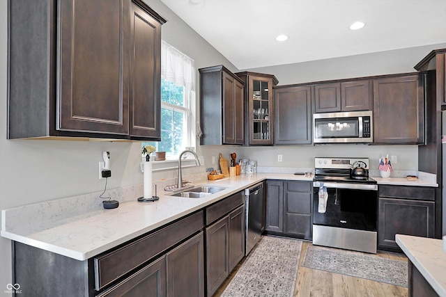 kitchen featuring recessed lighting, appliances with stainless steel finishes, glass insert cabinets, a sink, and dark brown cabinetry