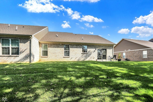 rear view of property featuring roof with shingles, brick siding, a lawn, and a patio