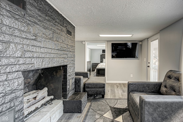 living room featuring a textured ceiling, light hardwood / wood-style flooring, and a stone fireplace