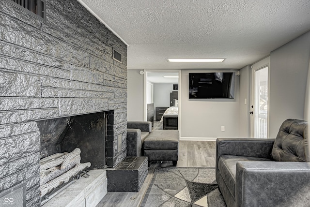 7587 Shady Side Dr, Bloomington, IN 47401 - living area featuring a textured ceiling, visible vents, a large fireplace, baseboards, and wood finished floors